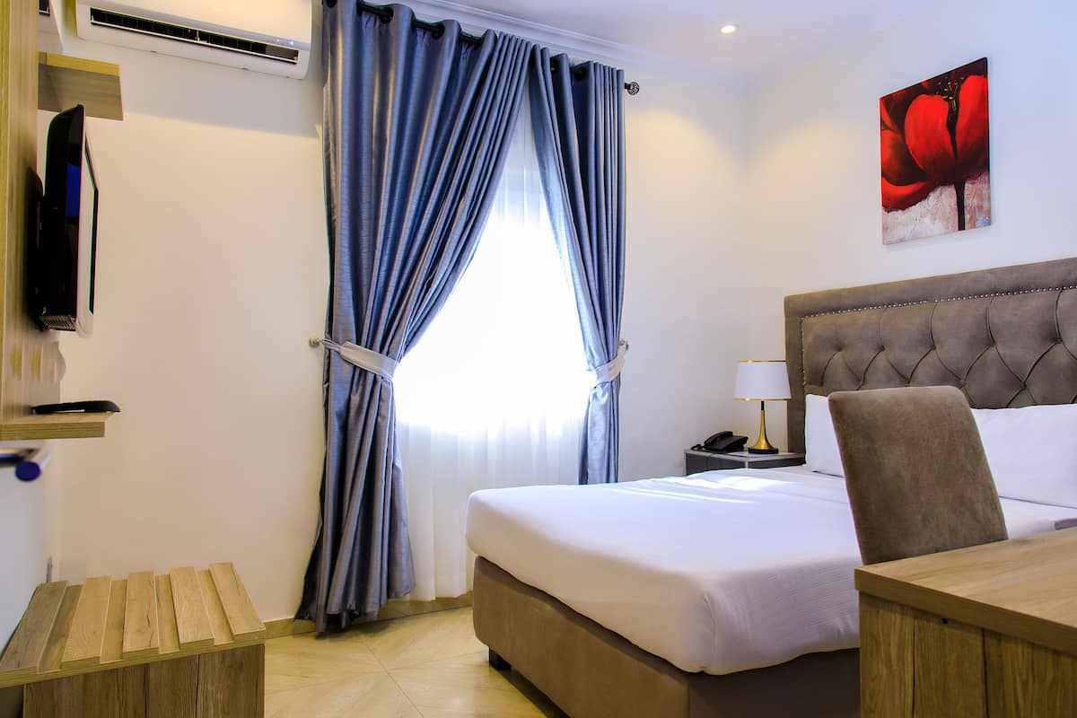 A hotel room with a bed, a desk, a chair, a lamp, and a painting on the wall.