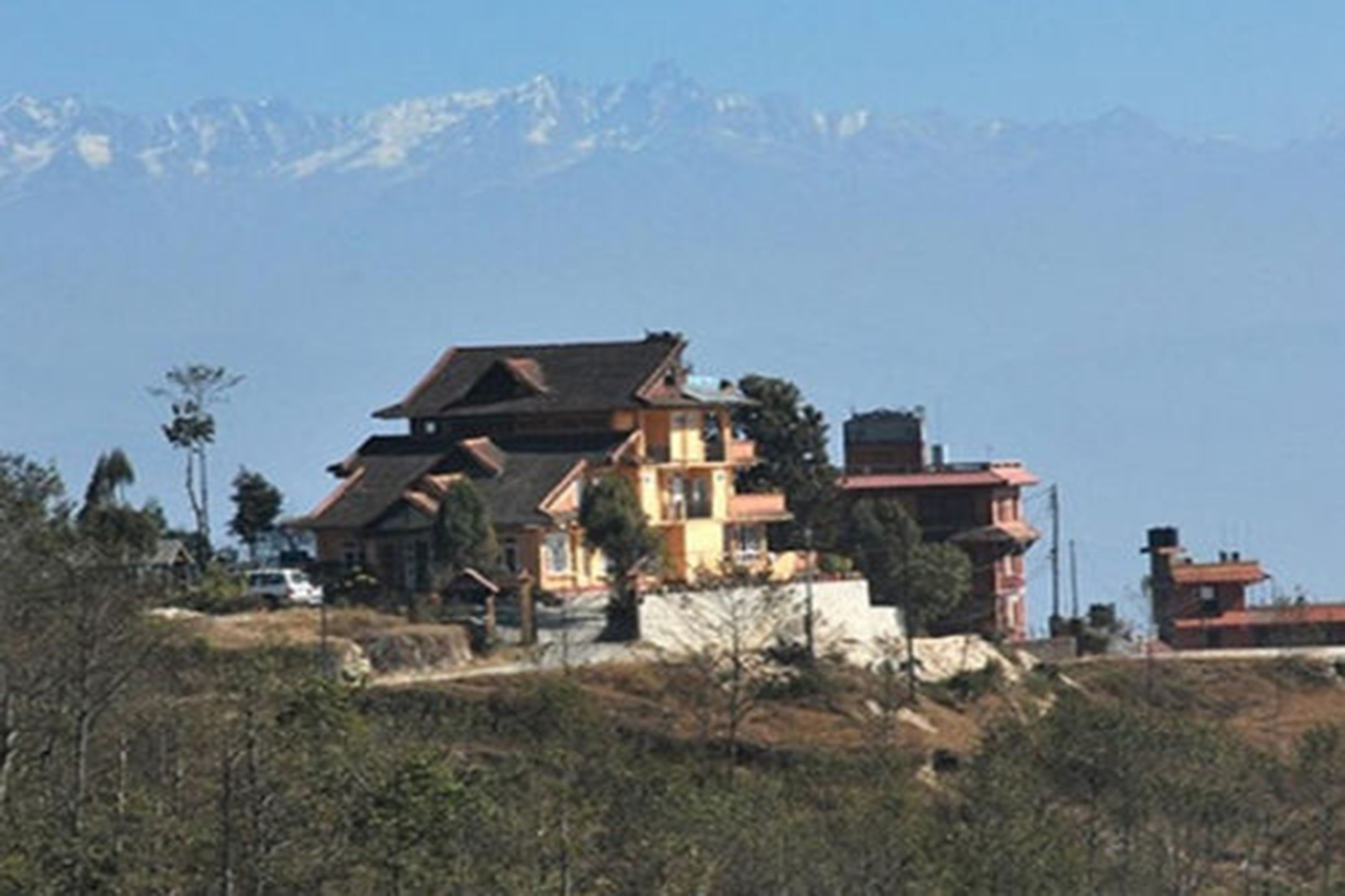 A house with a sloped roof and a chimney, surrounded by a hilly landscape with mountains in the background.