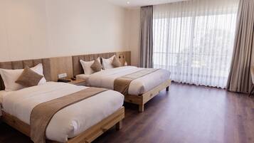 Quarto de hotel com duas camas de madeira, uma janela grande com cortinas finas e piso de madeira.