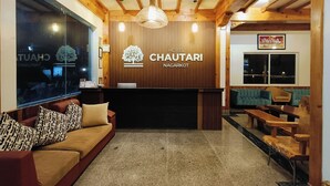 Een hotel lobby met een receptiebalie, houten balken in het plafond, een grote kroonluchter, een bank met gestreepte kussens, en een zithoek met houten banken.