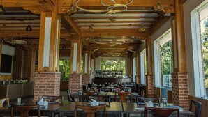 Een ruim restaurant met hoge houten plafonds, meerdere hangende lampen, bakstenen zuilen en grote ramen voor natuurlijk licht.