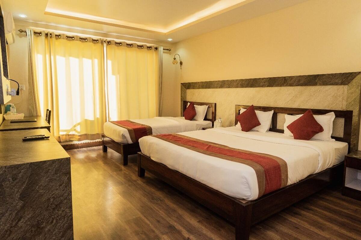 Habitación de hotel con dos camas, cabeceros de madera, encimera de mármol y un ventanal con cortinas.