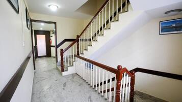 Um corredor com piso de mármore que leva a uma escadaria com guarda-corpo de madeira e corrimão branco.