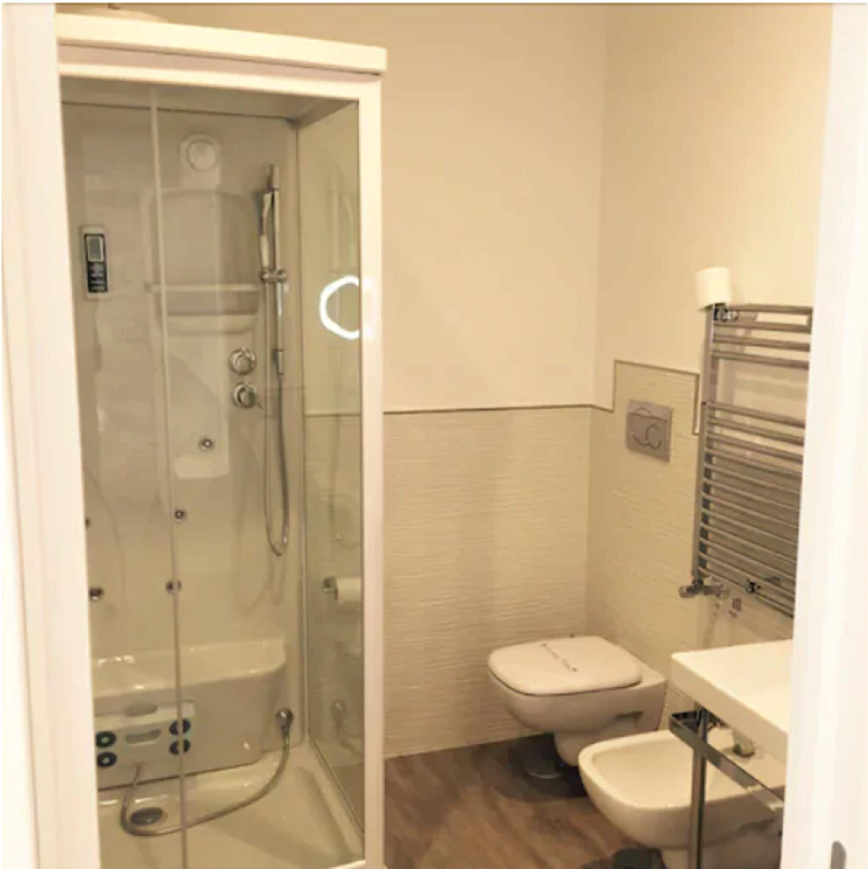 A bathroom with a glass-enclosed shower, a toilet, and a sink.