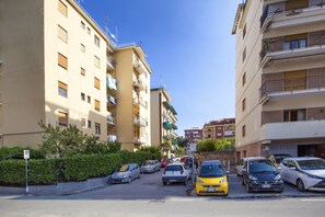 A narrow street lined with multi-story residential buildings, parked cars, and a clear blue sky. - Vhome (Sorrento)