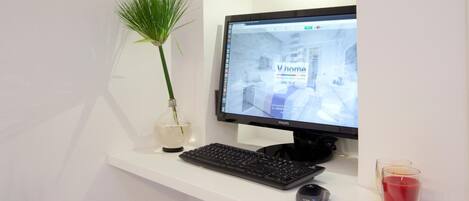 A computer monitor on a white desk with a keyboard and a mouse, a vase with a plant, and a candle.