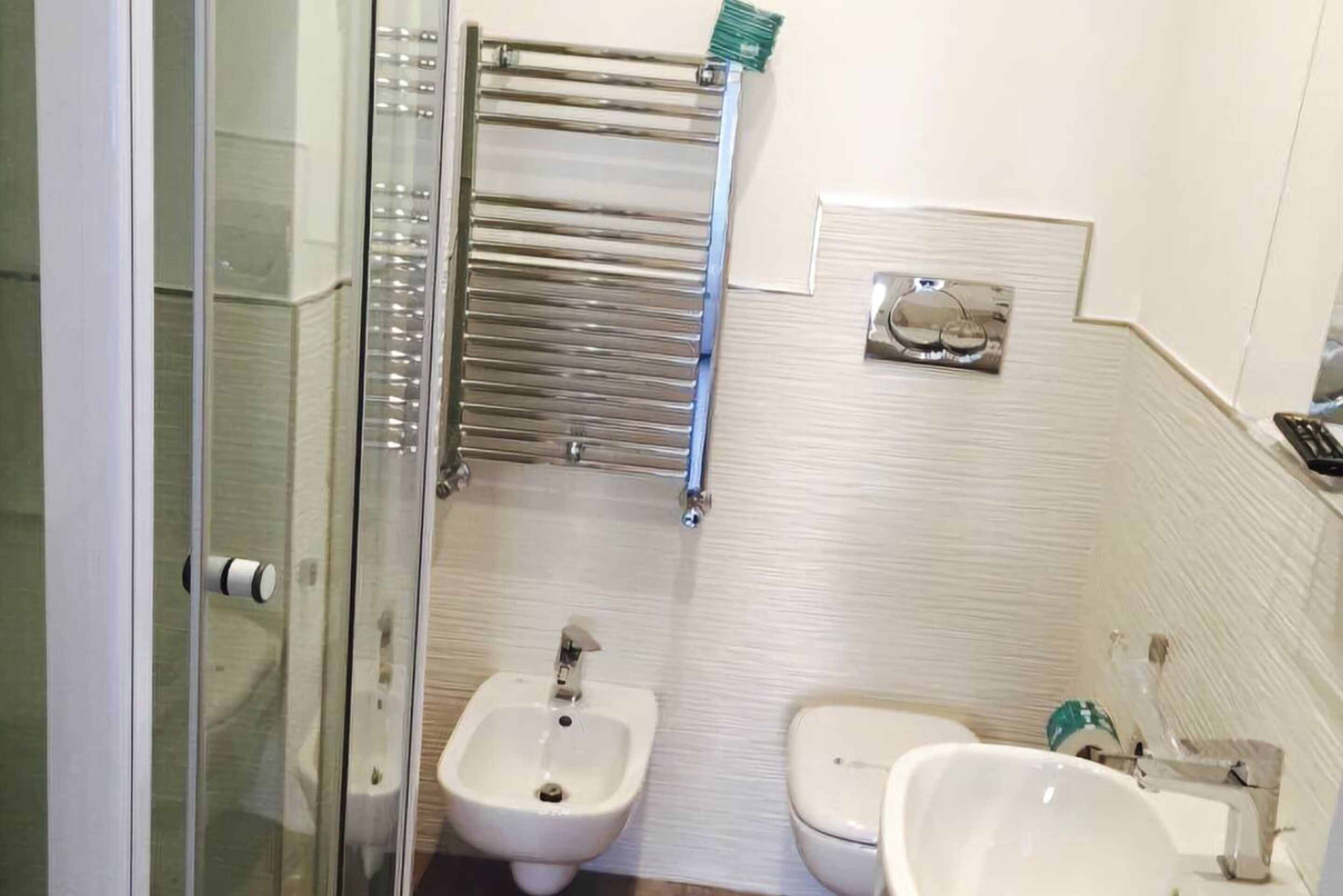 Un baño con bidé, inodoro, cabina de ducha de vidrio y perchero para toallas.