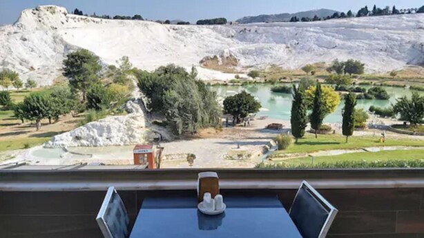Una habitación con una mesa, sillas y vistas a un paisaje natural con colinas y un cuerpo de agua.