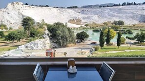 Una habitación con una mesa, sillas y vistas a un paisaje natural con colinas y un cuerpo de agua.