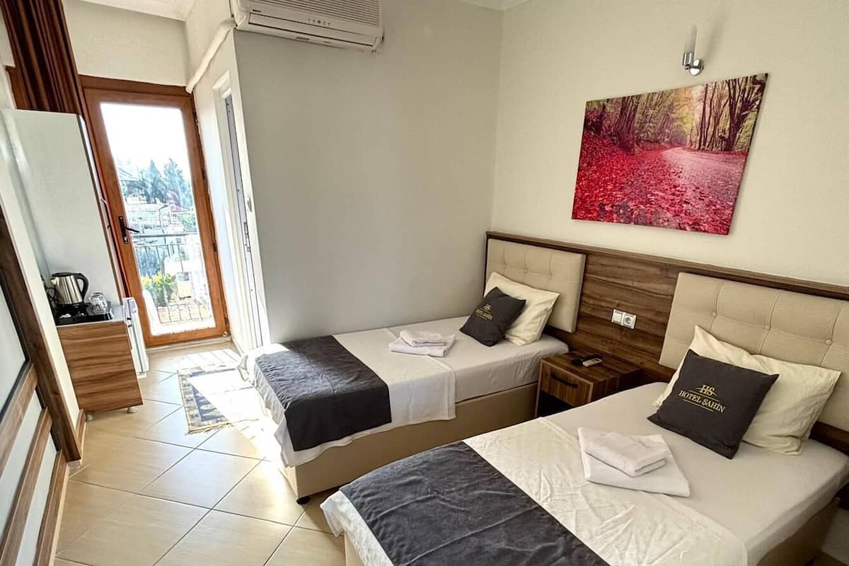 A hotel room with two beds, a large window, a ceiling fan, and a painting on the wall.