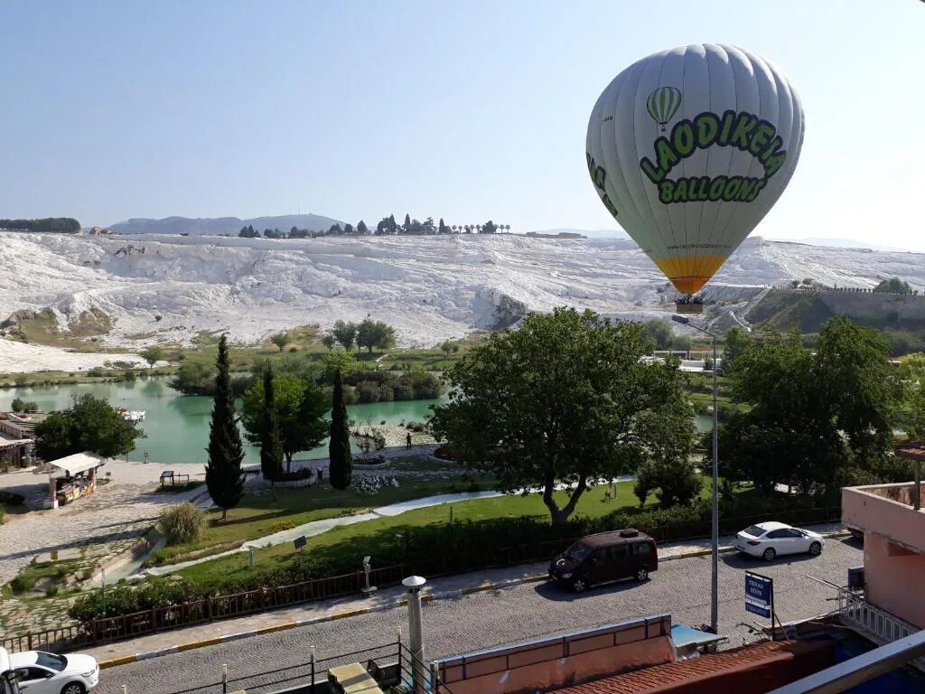 Un globo aerostático con la leyenda 'LAODIKEA BALLOONS', un cuerpo de agua, árboles y una carretera con vehículos.