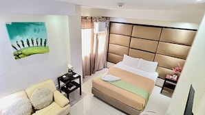 A hotel room with a bed, a sofa, a small table, a TV, and a painting on the wall. - Canberry Hotel (Cebu City)