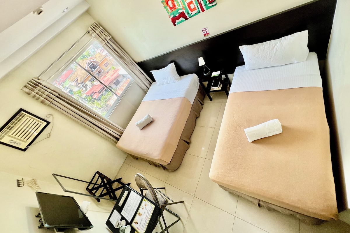 A hotel room with two beds, a window with curtains, a small table with a menu, and a chair.