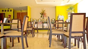 A dining area with multiple tables and chairs, a central floral arrangement, and a bright yellow wall. - Canberry Hotel (Cebu City)
