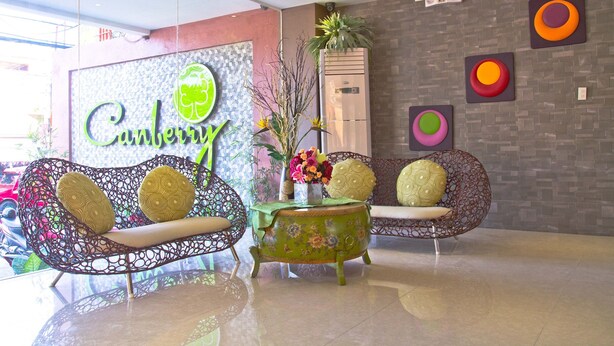 A reception area with two patterned sofas, a small table with a vase of flowers, and a wall with a 'Canberra' sign. - Canberry Hotel (Cebu City)