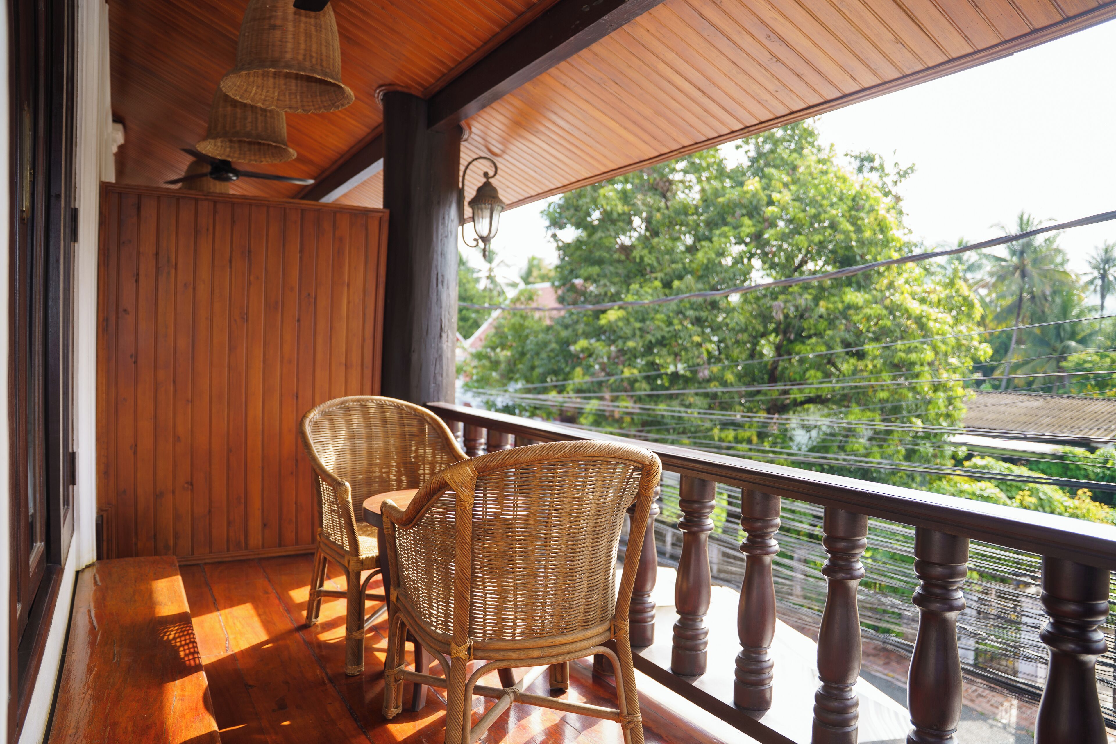 A wooden balcony with wicker chairs and a view of greenery.