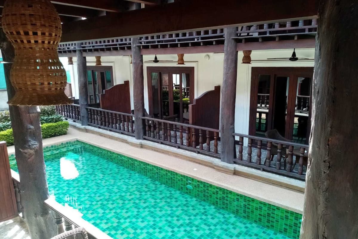 Un espace piscine doté d’un sol carrelé, de colonnes en bois et d’une rambarde.