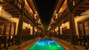 Une piscine au sol carrelé, entourée de rampes et de colonnes en bois, avec un éclairage d’ambiance nocturne.