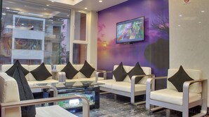 Un área de estar moderna con sofás y sillones blancos, una mesa de centro de vidrio y un televisor de pantalla plana montado en la pared.