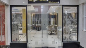 La entrada al Restaurante Royal South, con un diseño moderno, presenta puertas de vidrio y un área de comedor visible en su interior.