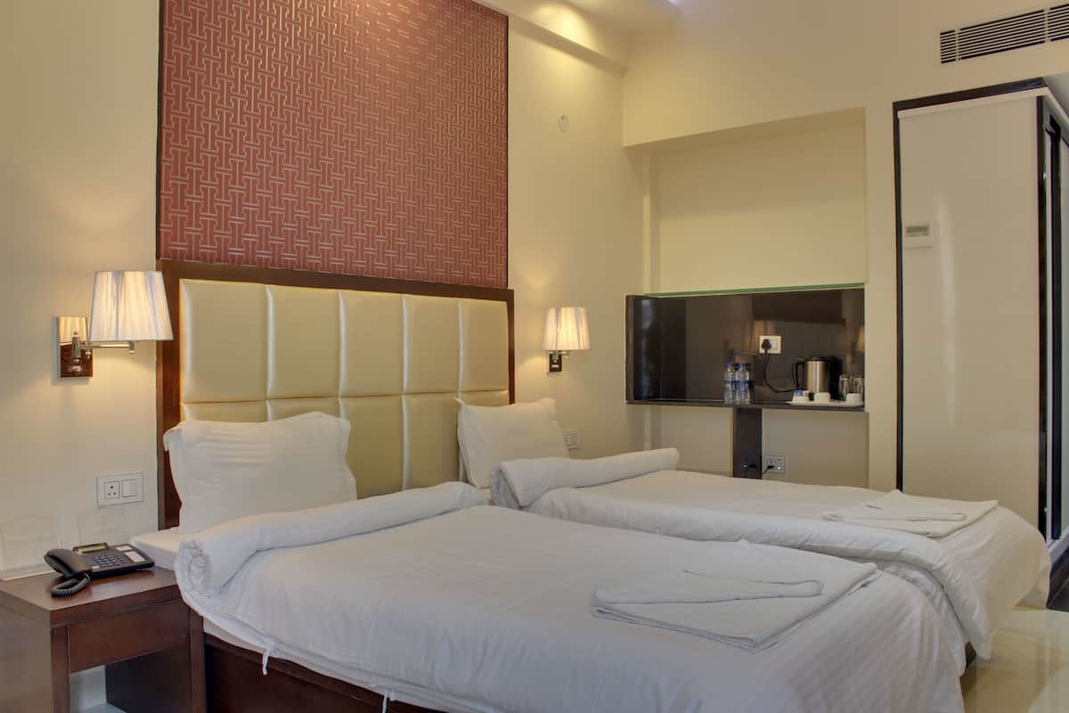 A hotel room with two beds, a nightstand with a phone and lamp, a mirror, and a minibar.