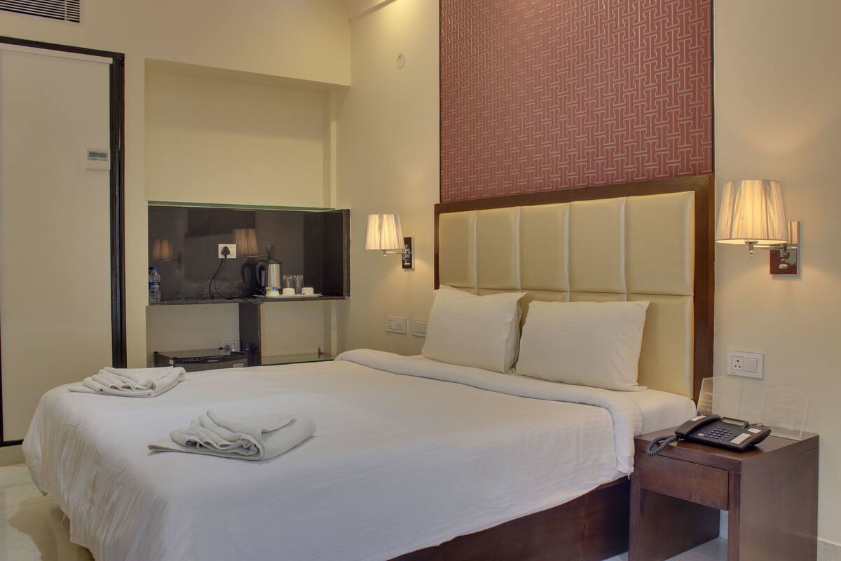 A hotel room with a large bed, a bedside table with a phone, and a mirror above the table.