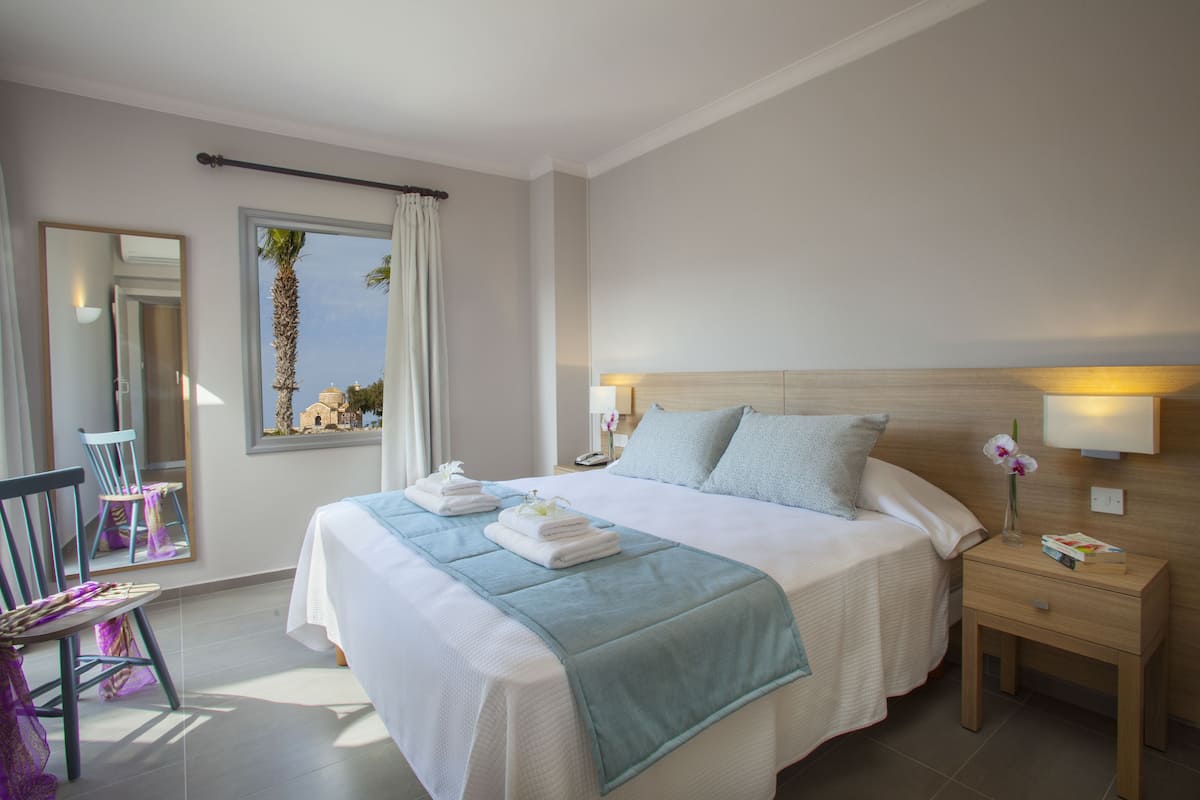 Uma cama bem arrumada com um edredom azul, uma mesa de cabeceira com abajur e uma cadeira com almofada roxa.