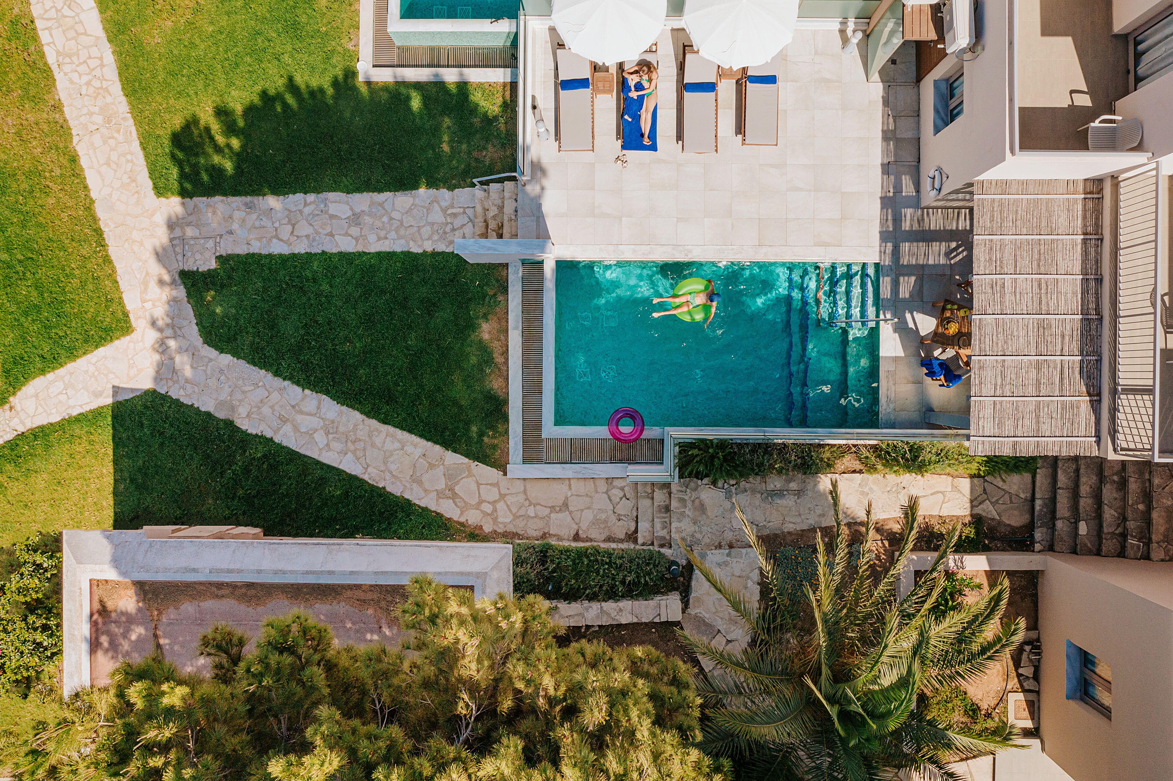 An aerial view of a swimming pool area with a stone pathway, lounge chairs, and a person swimming.