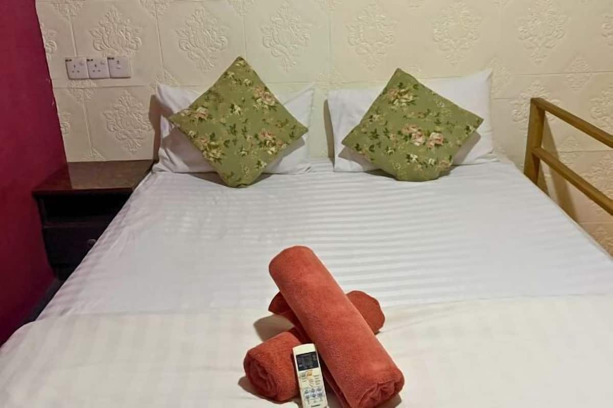 Un lit avec une literie blanche, deux coussins à motifs floraux verts et une serviette orange enroulée.