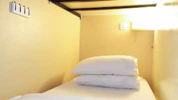 Una habitación pequeña con cama individual, pared amarilla lisa y cama sencilla con ropa de cama blanca.
