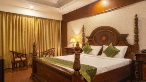A large wooden four-poster bed with green throw pillows, a wooden nightstand, and a chair.