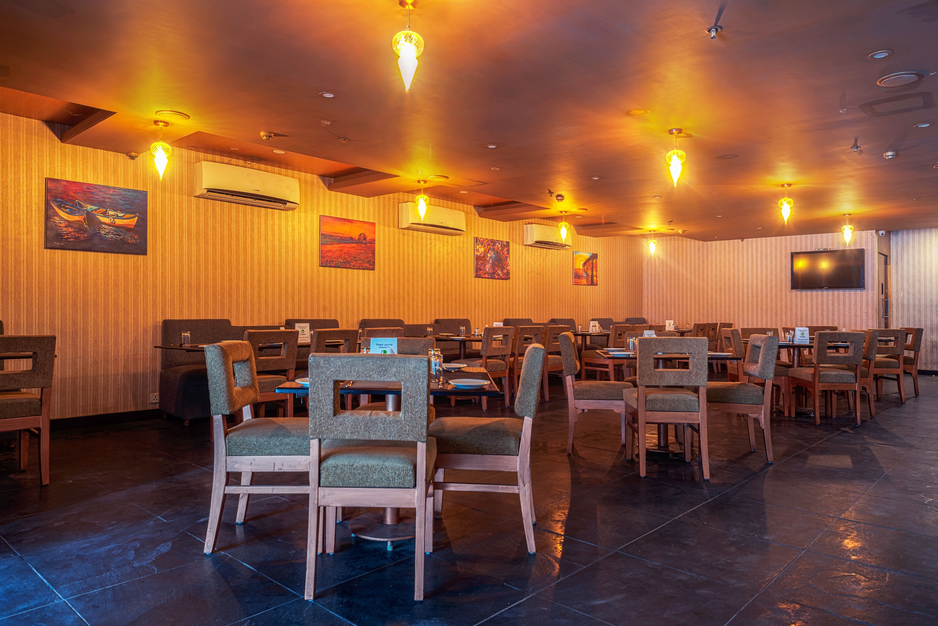 A conference room with multiple tables and chairs, air conditioning units, and wall-mounted artwork.