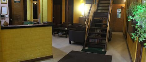 A hotel lobby with a reception desk, seating area, staircase, and a green plant.