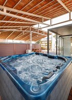 Un jacuzzi bajo una estructura de techo de madera con vista a un edificio moderno al fondo.
