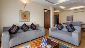 A modern living room with two grey sofas, patterned throw pillows, a wooden coffee table with water bottles, and a framed abstract painting on the wall. - Shaligram Hotel (Lalitpur)