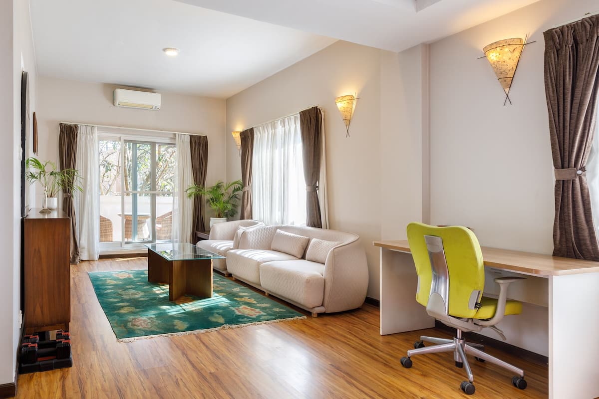A modern living room with a sofa, a desk with a chair, a glass coffee table, and a green rug.