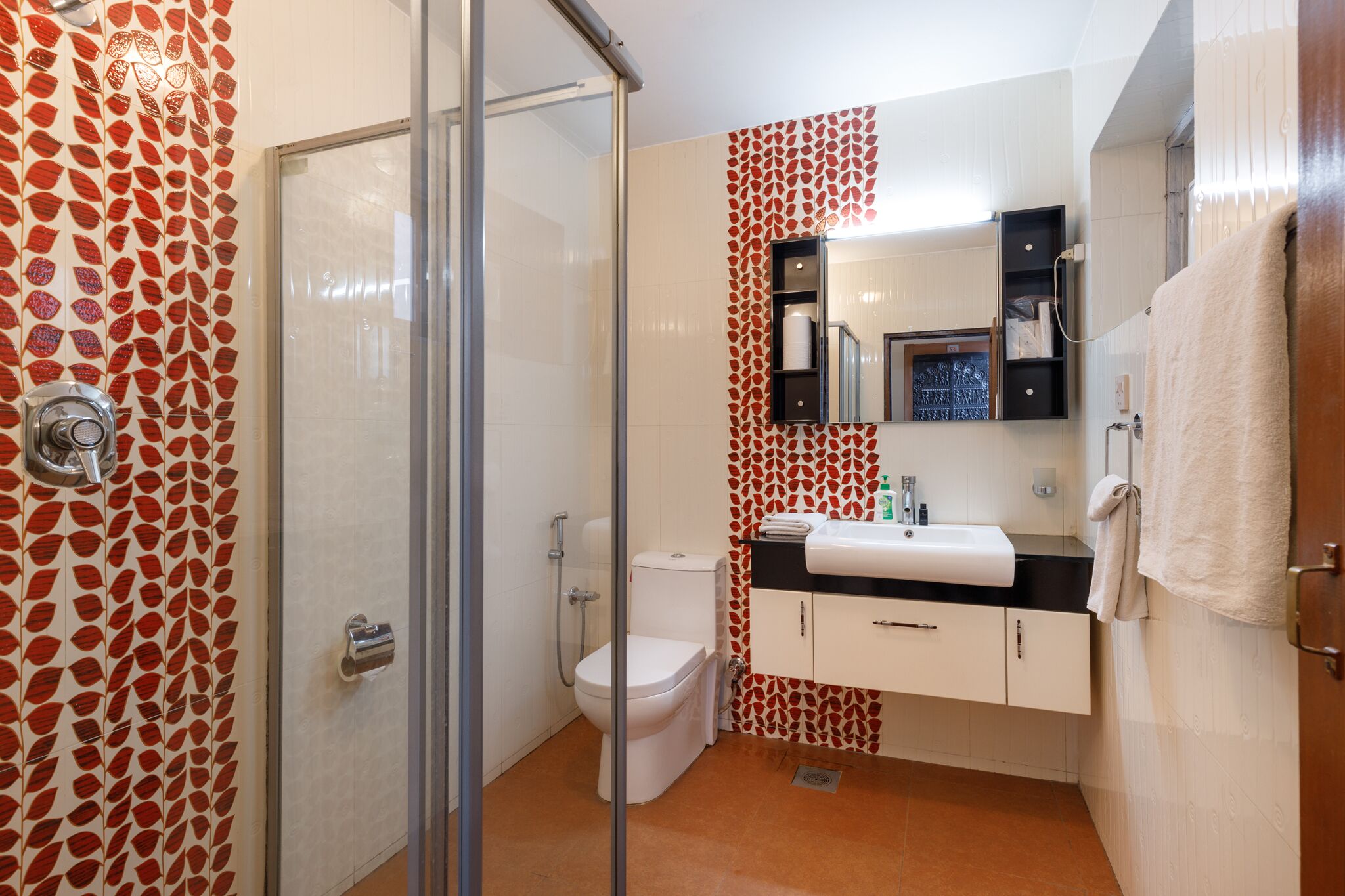A bathroom with a glass shower enclosure, a toilet, a sink with a mirror, and a towel rack.