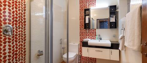 Un baño con cabina de ducha de vidrio, inodoro, lavamanos con espejo y toallero.