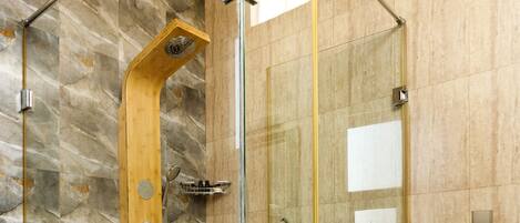 Un baño moderno con ducha envuelta en cristal, tocador de madera y pared con azulejos de mármol.