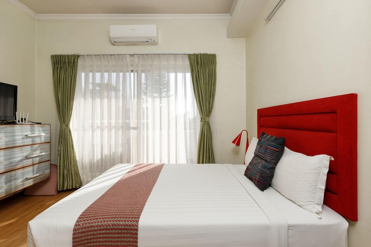 A hotel room with a bed, a TV, a dresser, and a window with curtains.