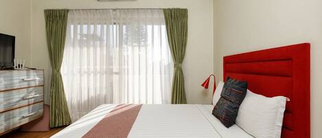 Habitación de hotel con cama, televisor, cómoda y ventana con cortinas.