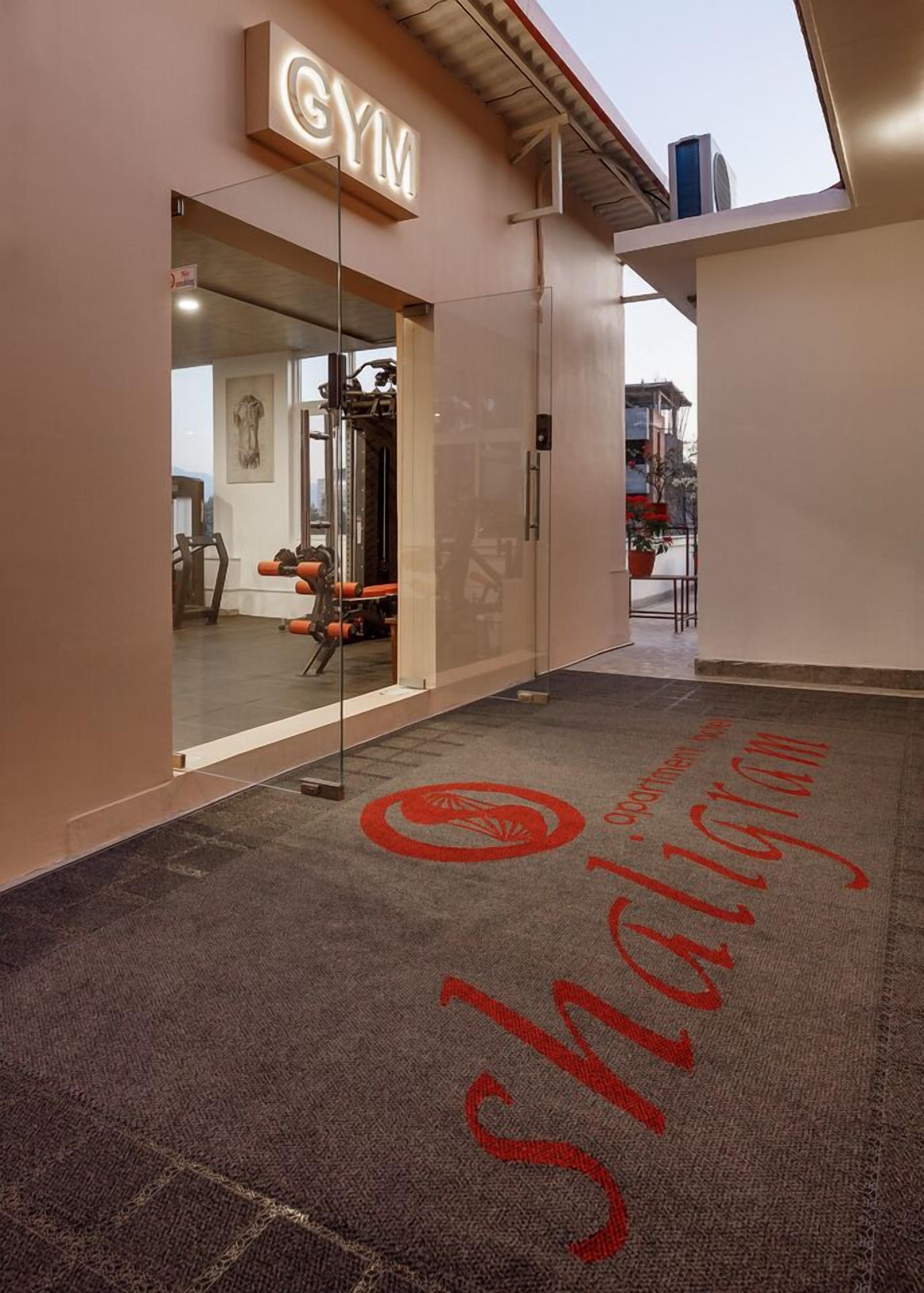 Een gym ingang met een glazen deur, een bord erboven en een vloerkleed met een logo.