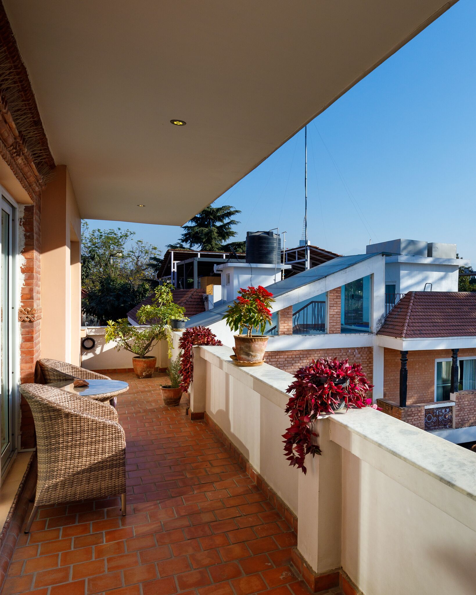 A balcony with wicker furniture, potted plants, and a view of neighboring buildings.