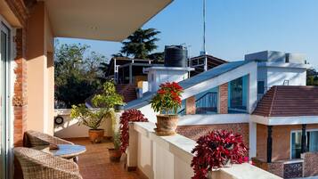 A balcony with wicker furniture, potted plants, and a view of neighboring buildings.