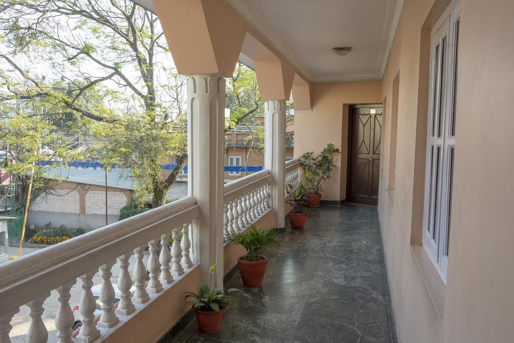 A covered balcony with a white balustrade, potted plants, and a view of buildings and trees.