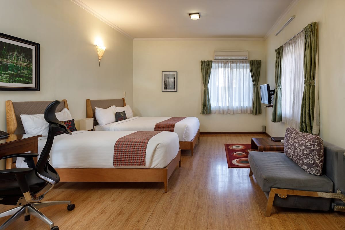 A hotel room with two beds, a desk, a chair, a sofa, and a TV.