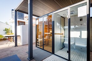 Un edificio moderno con puerta de entrada de vidrio, techo de madera y un interior visible con escalera y zona de estar.