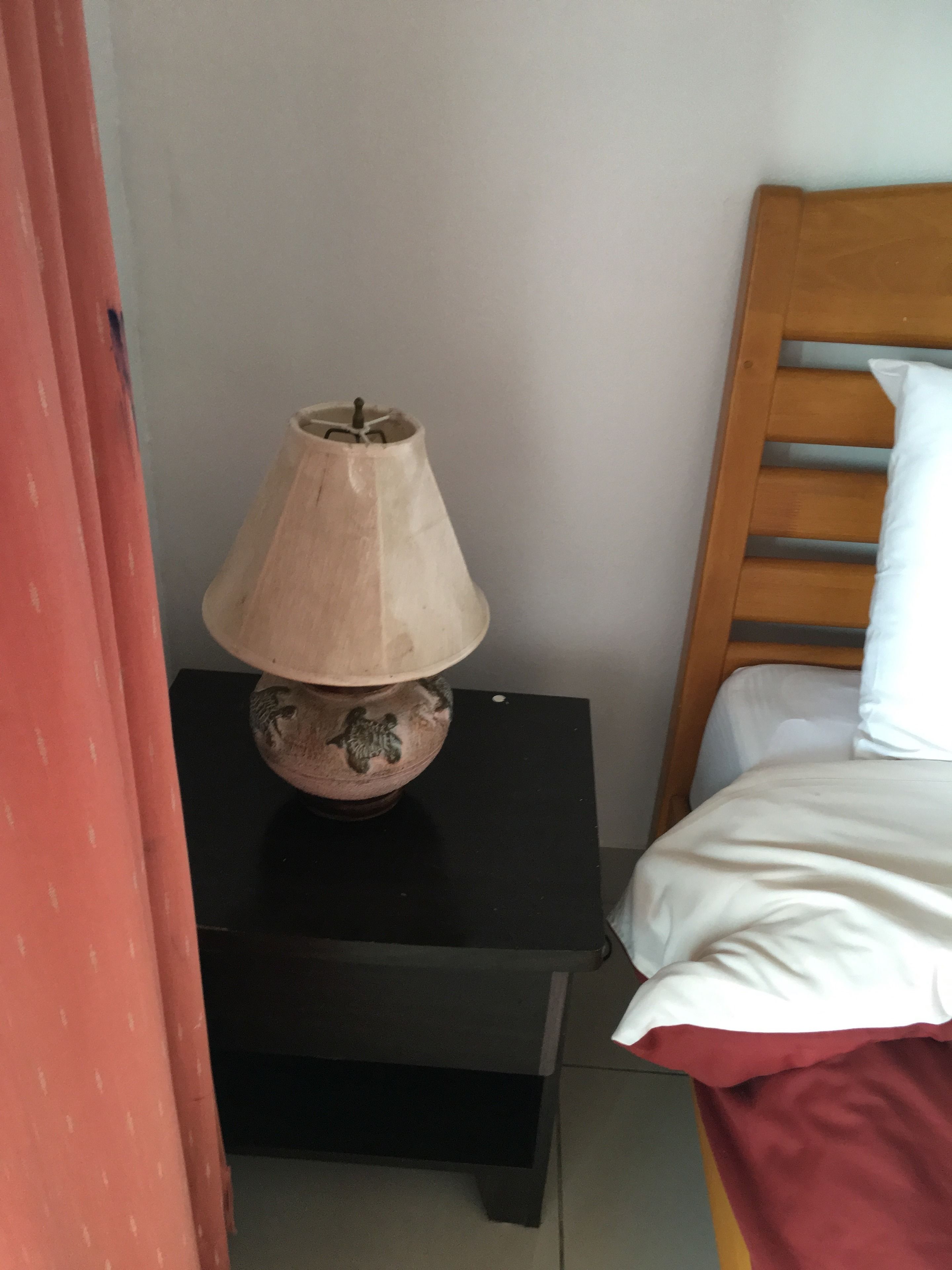 A bed with a wooden headboard, a nightstand with a lamp, and a red curtain.