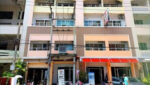 Un edificio de varios pisos con toldo rojo, un letrero que anuncia alquiler de motocicletas y varias motocicletas estacionadas.