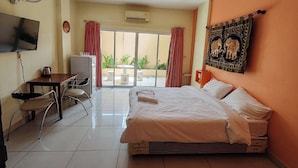 Habitación de hotel con cama, escritorio, silla, televisor y puerta corrediza de vidrio a un espacio exterior.